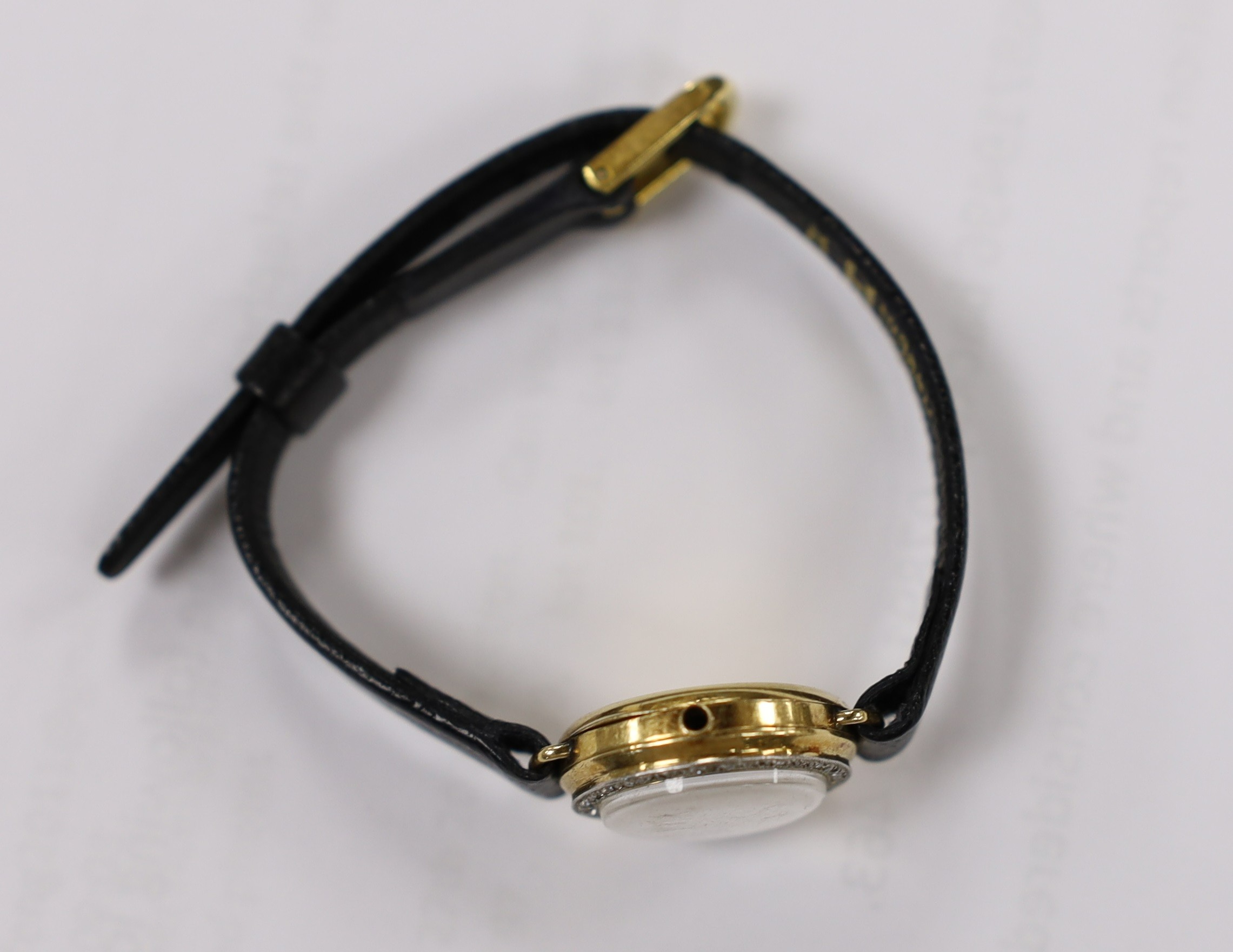A lady's 18k manual wind wrist watch, with diamond set bezel and dial with baton numerals (a.f.), on a leather strap, lacks winding crown.